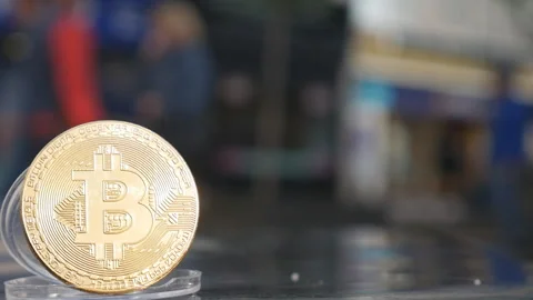 A gold Bitcoin with people walking in the background. Stock Footage 125948028