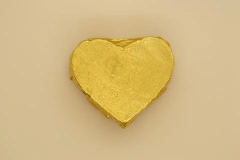 Gold candy wrapper in the shape of a heart on a light beige background. 스톡 사진