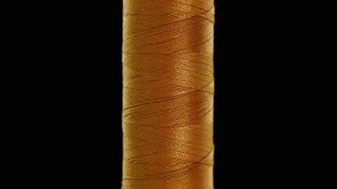Gold colored sewing thread on a black background Stock Footage 147562351