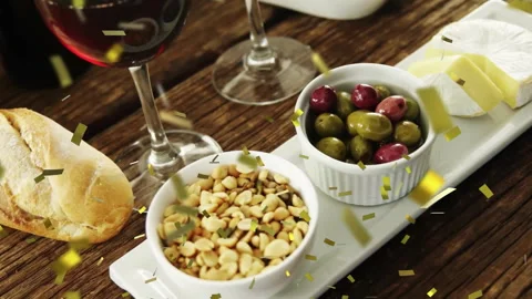 Gold confetti dropping falling swirling around bread wine olives cheese in tray 動画素材 313704436