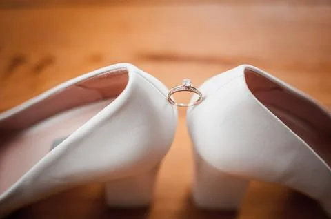 Gold diamond ring between pair of white high heel shoes Stock Photos