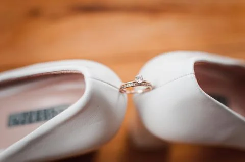 Gold diamond ring between pair of white high heel shoes Stock Photos