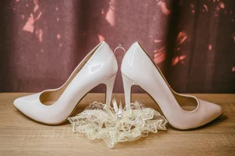 Gold diamond ring between pair of white high heel shoes. Wedding details on r Stock Photos