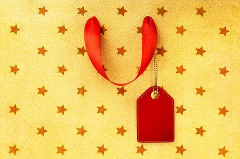 Gold glitter star pattern background with red ribbon handle and blank gift ta Stock Photos
