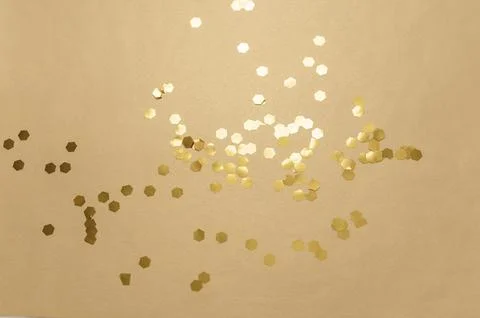 Gold hexagonal glitter particles scattering on a warm beige background, symbo Stock Photos