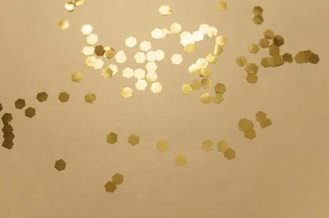 Gold hexagonal glitter particles scattering on a warm beige background, symbo Stock Photos