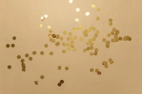 Gold hexagonal glitter particles scattering on a warm beige background, symbo Stock Photos