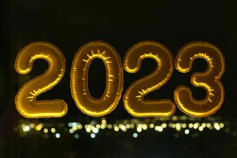 Gold inflatable foil balloons numbers 2023 on the window against the background Stock Photos