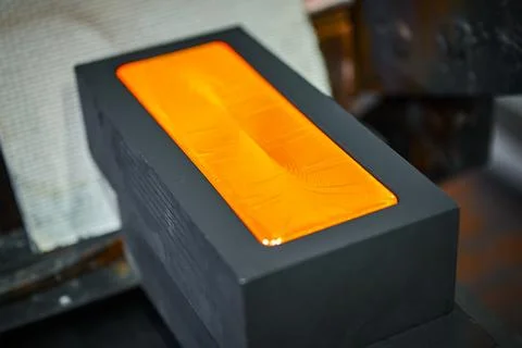 Gold ingot in graphite casting form on workbench at plant Stock Photos