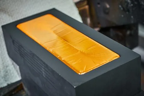 Gold ingot in graphite casting form on workbench at plant Stock Photos
