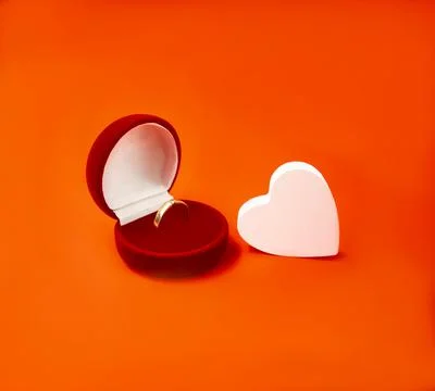 A gold ring with in a gift box and a wooden, white heart on a red background Stock Photos