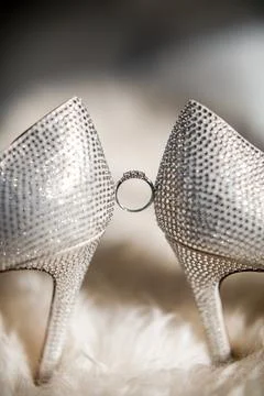 A gold ring hangs between wedding shoes Stock Photos