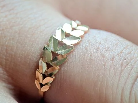 Gold ring worn on a finger, featuring leaf-shaped links, photographed indoo.. Stock Photos