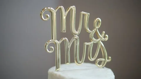 Gold script Mr and Mrs letters on top of white wedding cake for Stock Footage 134583201