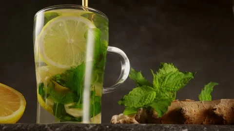 Gold spoon stirring ginger tea with lemon and mint in glass cup on black Stock Footage 136961771