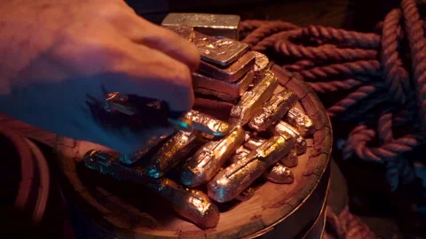 Gold treasure piled up on a barrel top. Hand enters from left, grabs an ingot Stock Footage 344058347