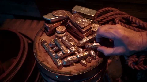 Gold treasure piled up on a barrel top. Hand grabs an ingot and examines it. Stock Footage 344059625