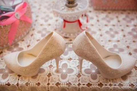 Gold wedding ring between pair of a white shoes Kerosene lamp background . El Stock Photos