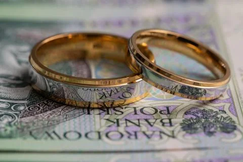 Gold wedding rings surrounded by a stack of Polish banknotes. Fotos Stock