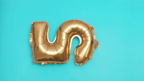 Golden balloon in the shape of five flies and falls on blue surface at birthday Stock Footage 232976320