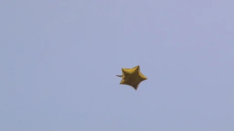 A golden balloon in the shape of a star flies in the sky Stock Footage