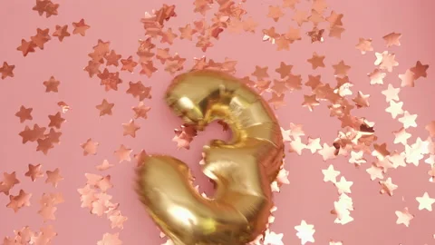 Golden balloon in shape of three flies and falls on the pink stars background at Stock Footage 232976485