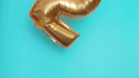 Golden balloon in the shape of two flies and falls on blue surface at birthday Stock Footage 214452720
