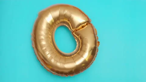 Golden balloon in the shape of zero flies and falls on blue surface at birthday Stock Footage 215088360