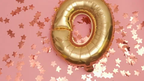 Golden balloons in the shape of zero falls on pink floor with stars Stock Footage 232976390