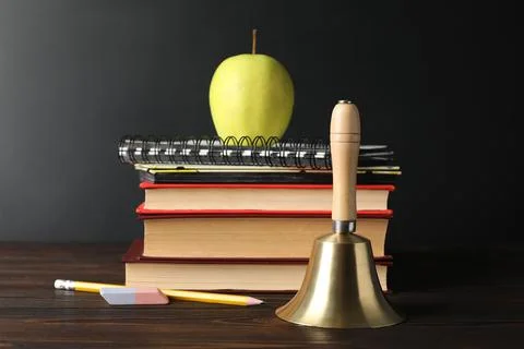 Golden bell, apple and school stationery on wooden table near blackboard Stock Photos