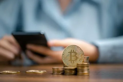 Golden bitcoin and stack of coin on wooden table with human using mobile phon Stock Photos
