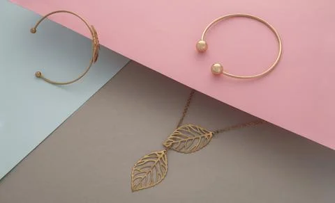 Golden bracelets and leaf shape necklace pendant on pastel colors paper backg Stock Photos