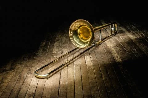Golden brass instrument trombone lies on a dark brown wooden stage in the ray Stock Photos