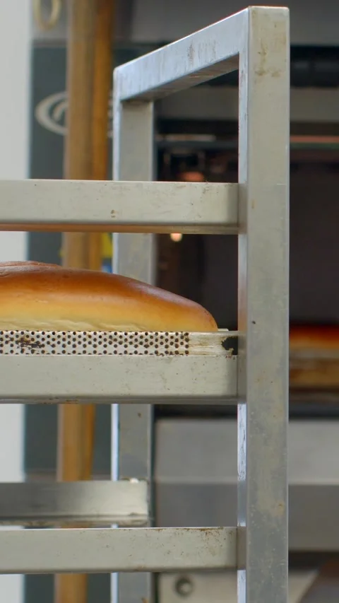 Golden bread loaves moving through stainless steel bakery rack and oven lip Видео 344576742