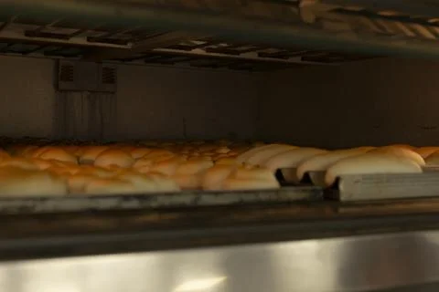 Golden bread rolls baking on conveyor in industrial oven with warm metal racks 스톡 사진