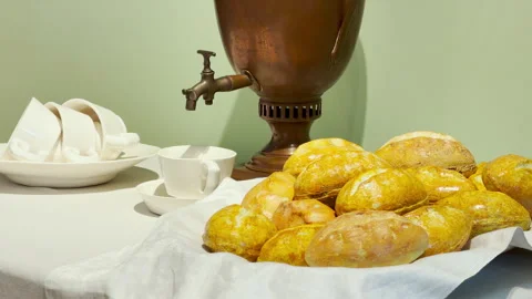 Golden bread rolls rest on a white napkin beside a samovar Stock Footage 344974633