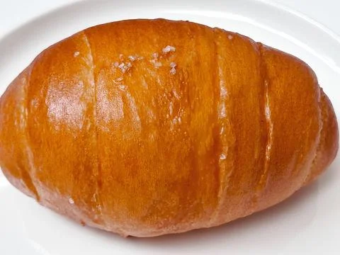 Golden-brown bread roll with coarse salt on a white plate. Stockfoto's