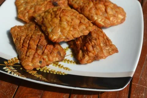 Golden brown fried Tempe on a patterned white plate. Stock Photos