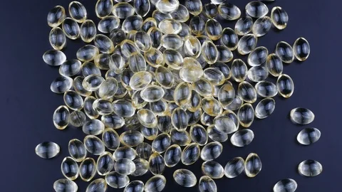 Golden capsules of vitamin D on a black background slowly rotate clockwise. Stock Footage
