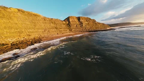 Golden cliffs meet crashing waves at sunrise Video stock 340914026