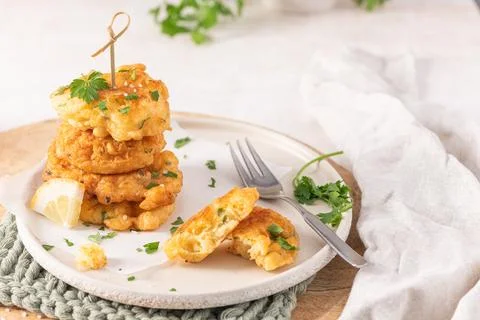 Golden cod fritters stacked on a rustic plate with fresh parsley and a lemo.. Stock Photos
