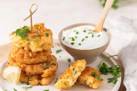 Golden cod fritters stacked on a rustic plate with fresh parsley and lemon .. Stock Photos