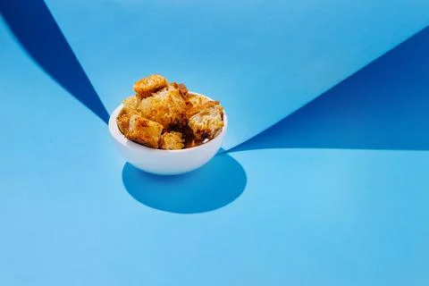 Golden crispy bread cubes in a white bowl against a blue backdrop creating .. Foto stock