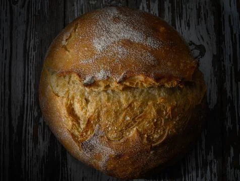 Golden crusted bread rests on a rustic wooden surface under soft warm lightin Stock Photos