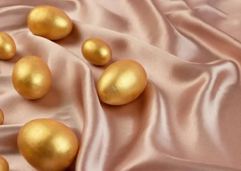 Golden decorative Easter eggs on a background of creamy shiny natural fabric 스톡 사진