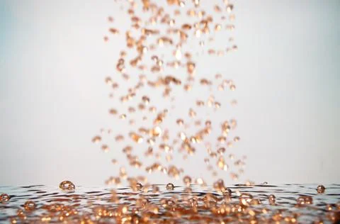 Golden drops of fluid fall to the surface of water Stock Photos
