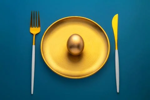Golden easter egg placed on a golden plate on a blue background, representing Stock Photos