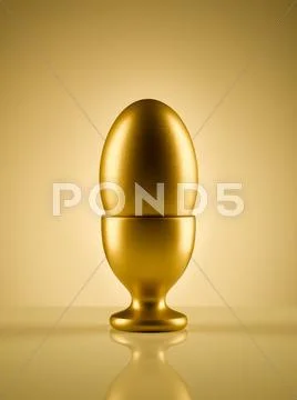Golden egg in egg cup holder against gold background Stock Photos