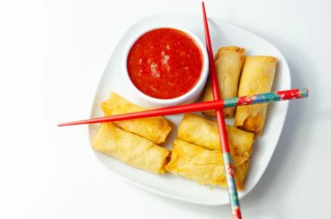 Golden egg rolls rest on a clean white plate Stock Photos