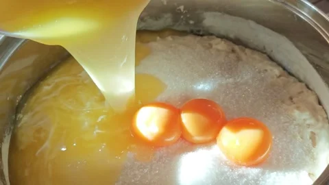 Golden egg yolks and egg whites pouring from a bowl into a stainless steel pot Stock Footage 346457638